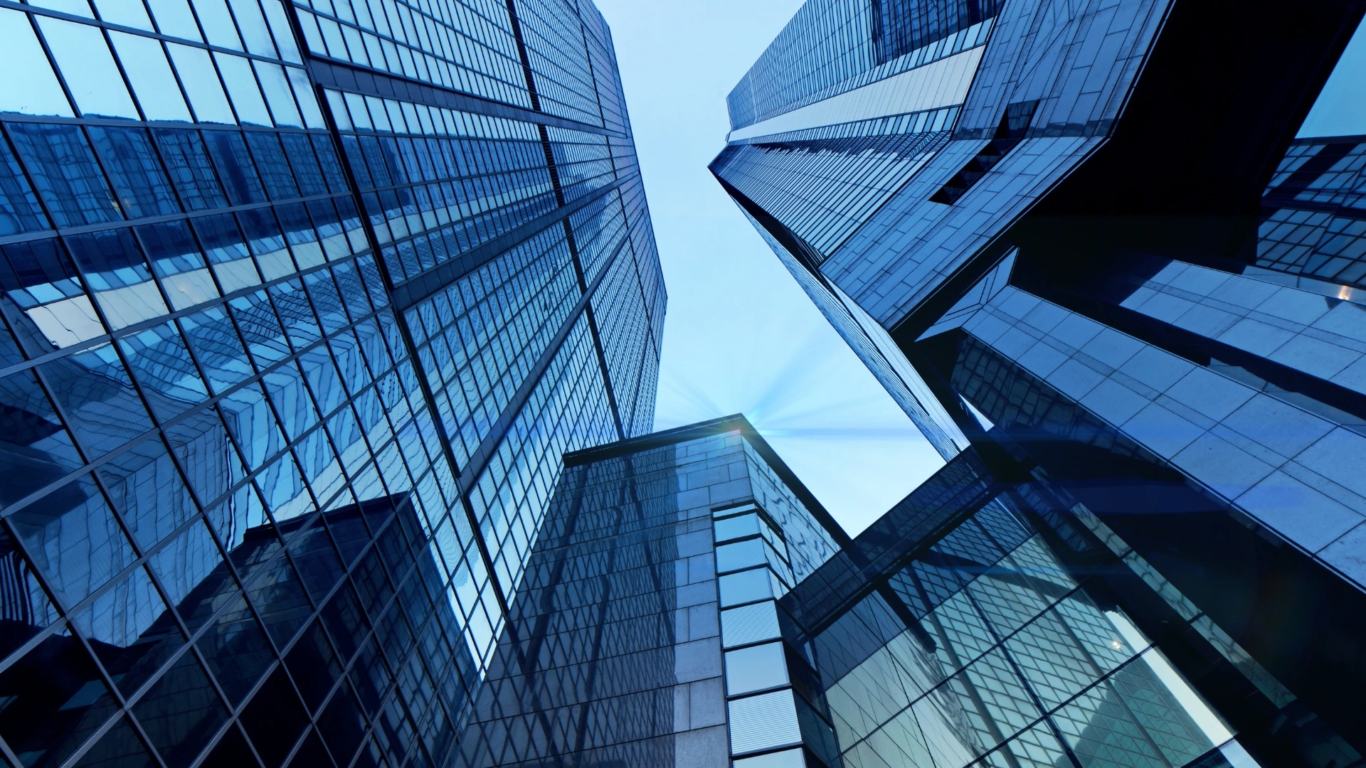Glass office towers photographed looking upward against a blue sky
