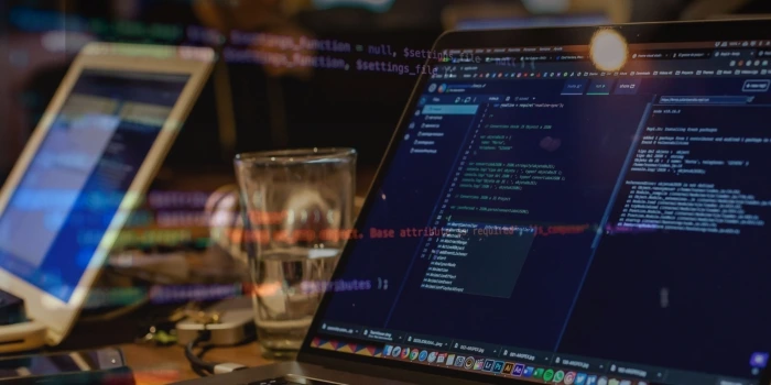 A laptop showing a code editor next to a tablet on a dark desk