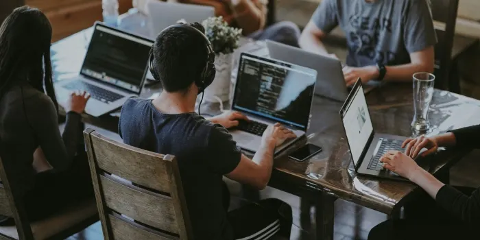Four people working on laptops around a wooden table